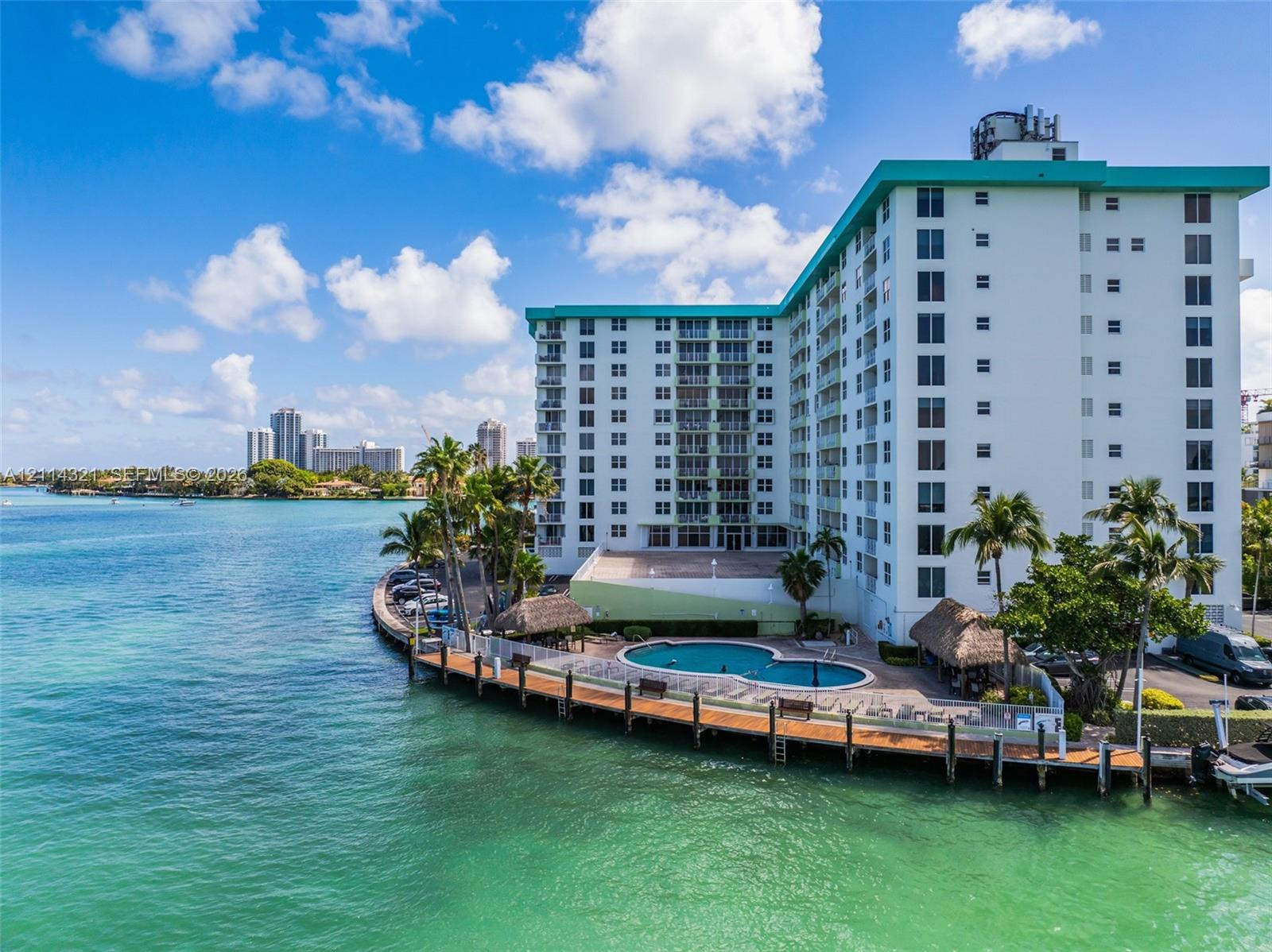 Waterfront multi-story building featuring an outdoor swimming pool, a perimeter wooden deck, and thatched-roof structures