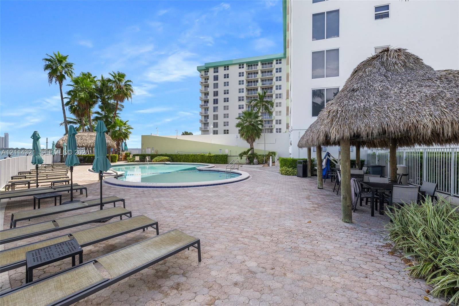 Swimming pool with a paved deck, thatched-roof cabana, and tropical landscaping
