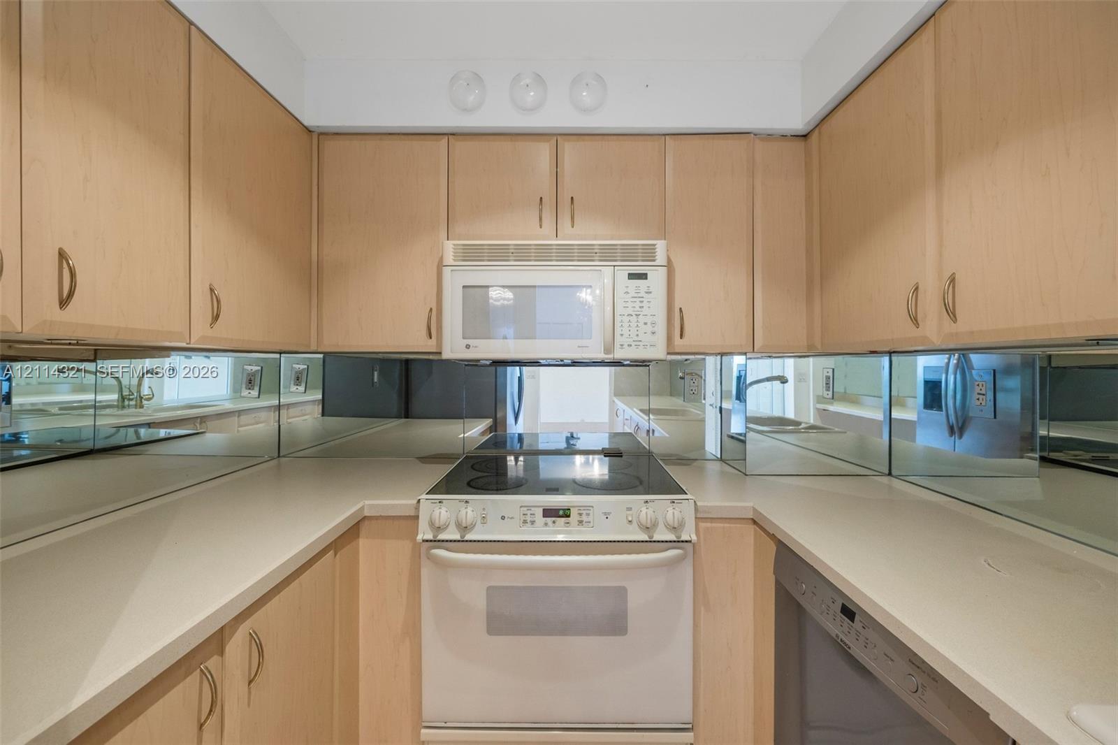 Kitchen featuring light wood-finish cabinetry, solid surface countertops, a mirrored backsplash, and a built-in over-the-range microwave