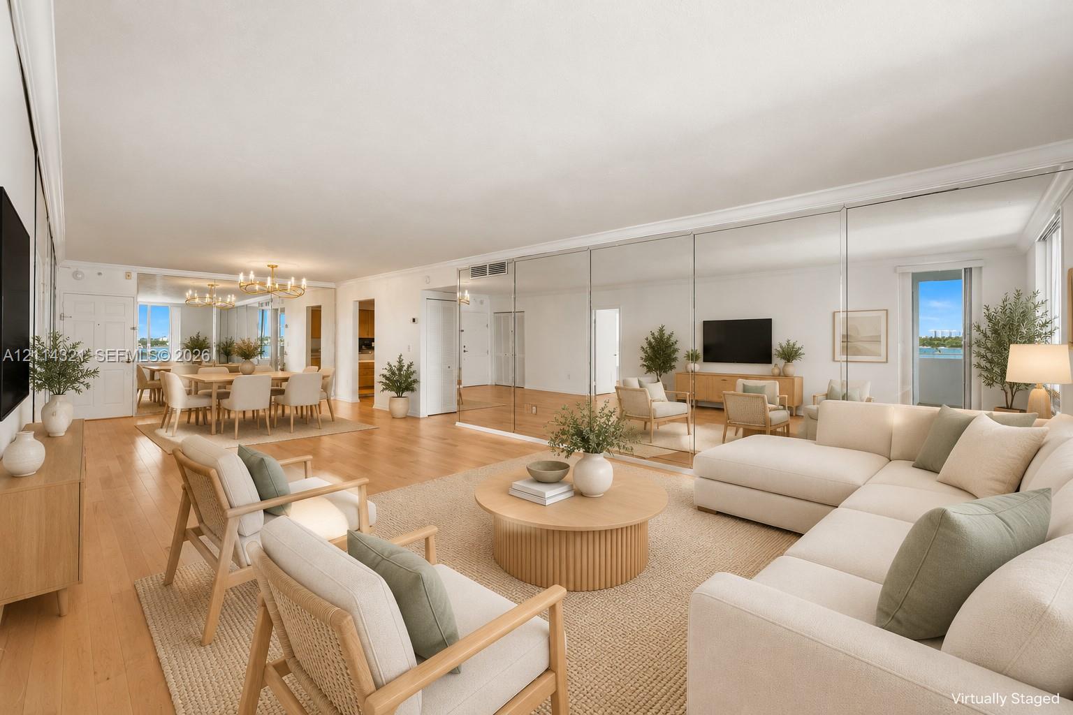 Expansive living area featuring light-toned wood-finish flooring, extensive mirrored wall paneling, and sliding glass doors
