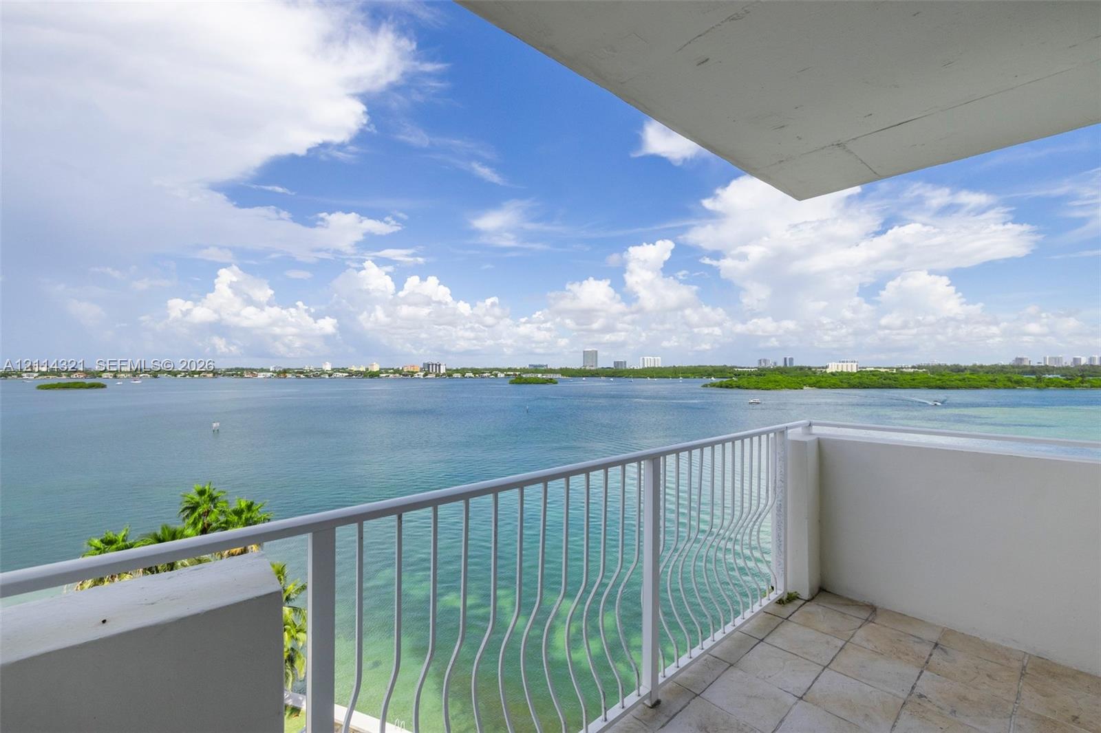 Private balcony featuring stone tile flooring and white metal railing overlooking an expansive bay and coastal horizon