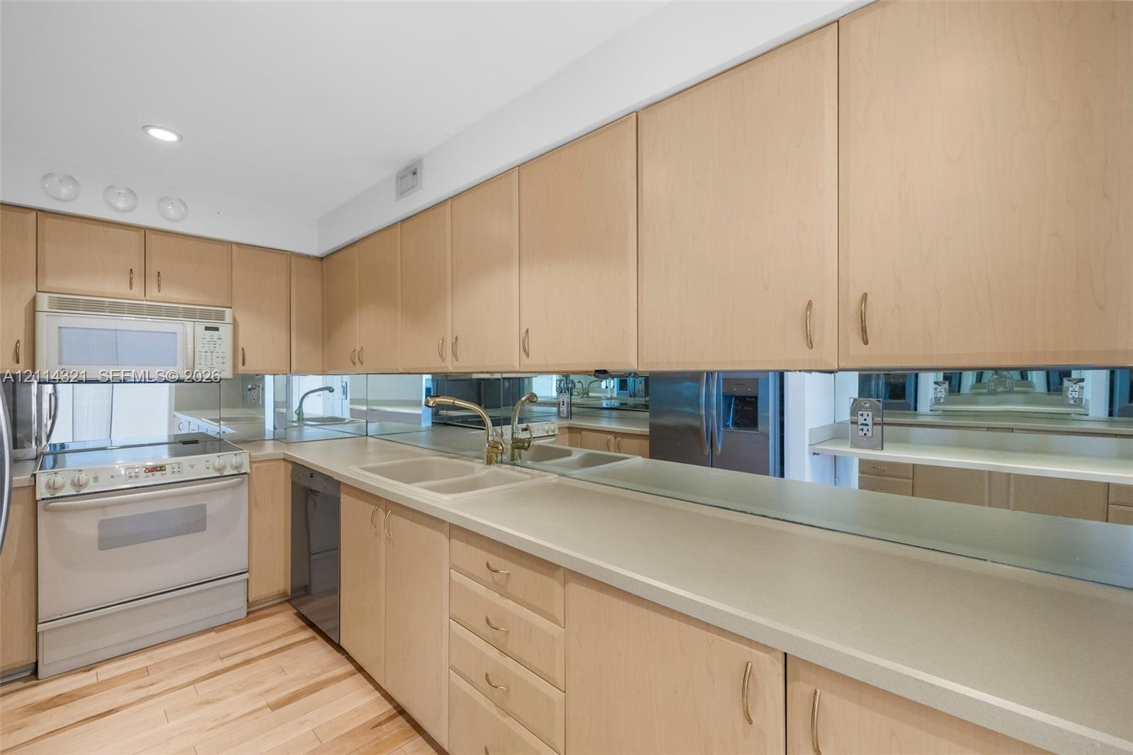 Kitchen featuring light-finish cabinetry, neutral solid-surface countertops, wood-finish flooring, a mirrored backsplash, and an integrated microwave