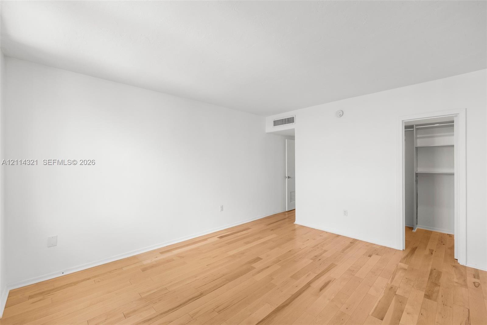 Neutral-toned interior featuring wood-finish flooring, white walls, and a walk-in closet with built-in shelving