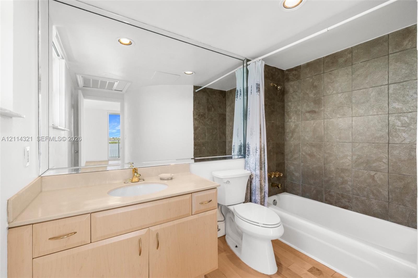 Bathroom featuring a vanity with an integrated countertop and sink, large wall-spanning mirror, wood-finish flooring, and a bathtub with tile surround