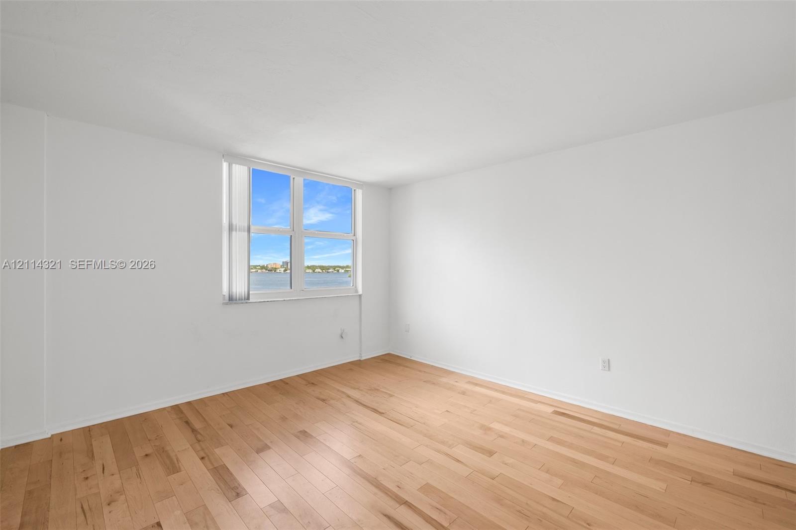 Interior room featuring light-toned wood-finish flooring, white walls, and a large window with white vertical blinds