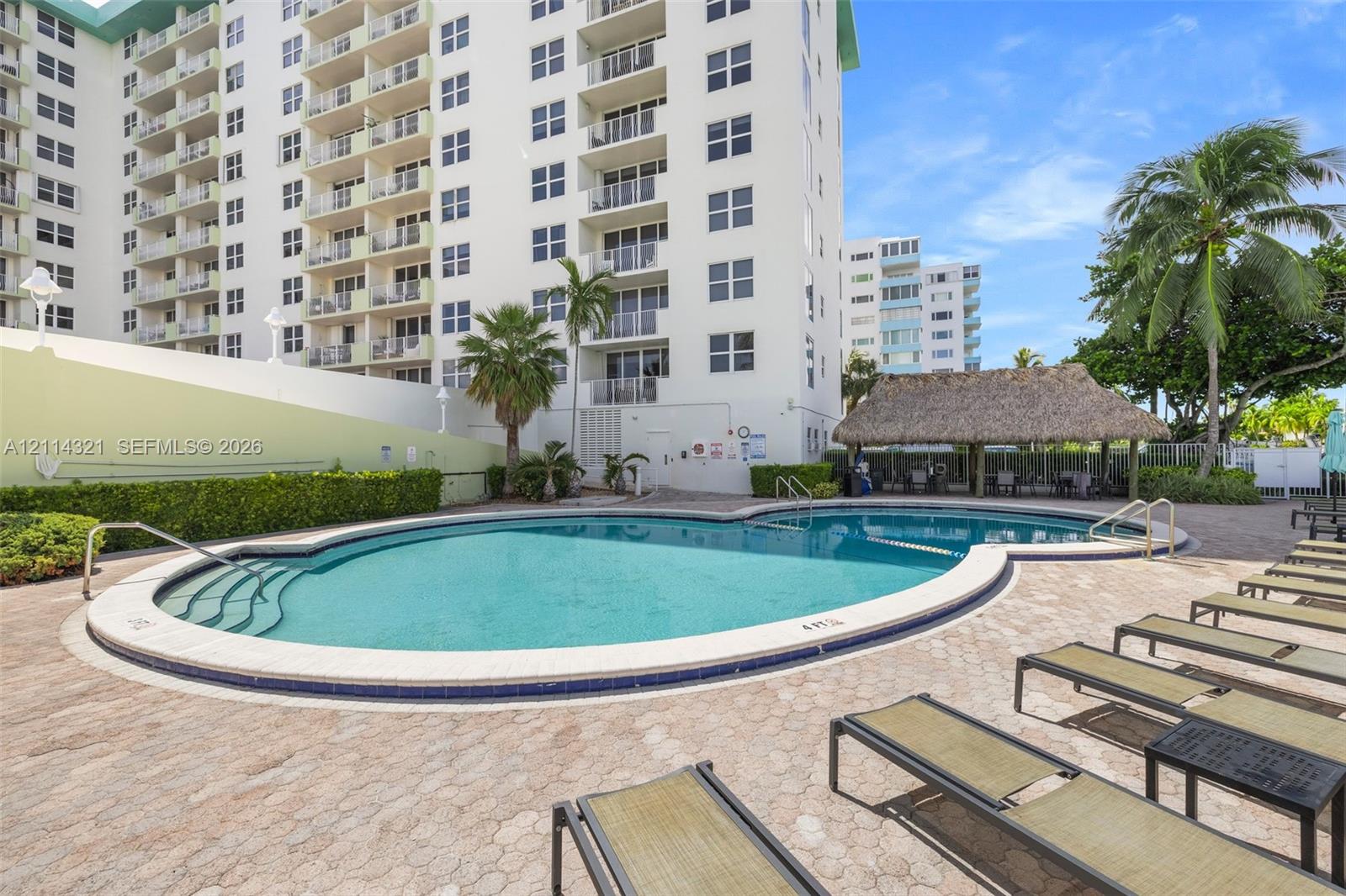 Curved outdoor swimming pool with built-in steps, paver pool deck, and thatched-roof tiki hut