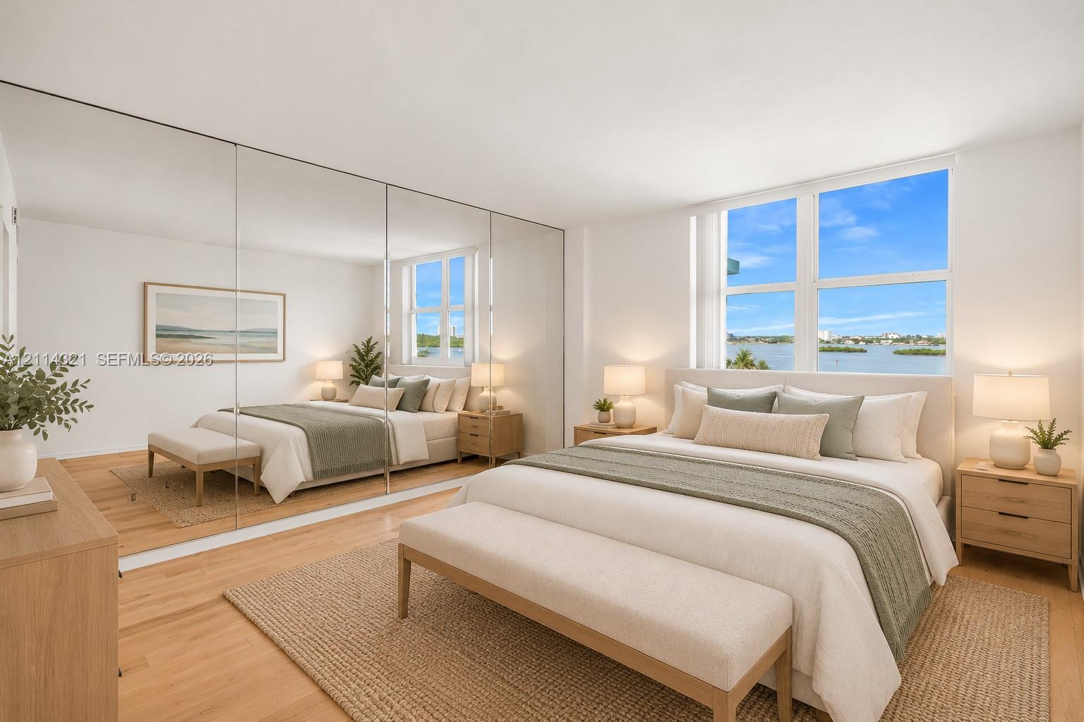 Floor-to-ceiling mirrored wardrobe doors, light-toned wood-finish flooring, and large windows with water scenery