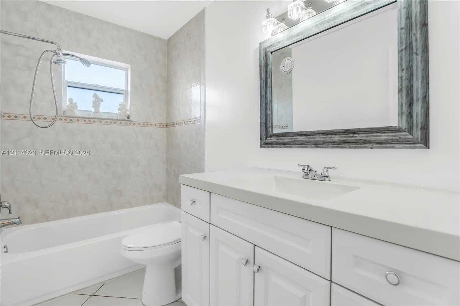 Bathroom featuring white cabinetry, solid-surface countertop, integrated vanity sink, wall-mounted mirror, and tile-surround tub