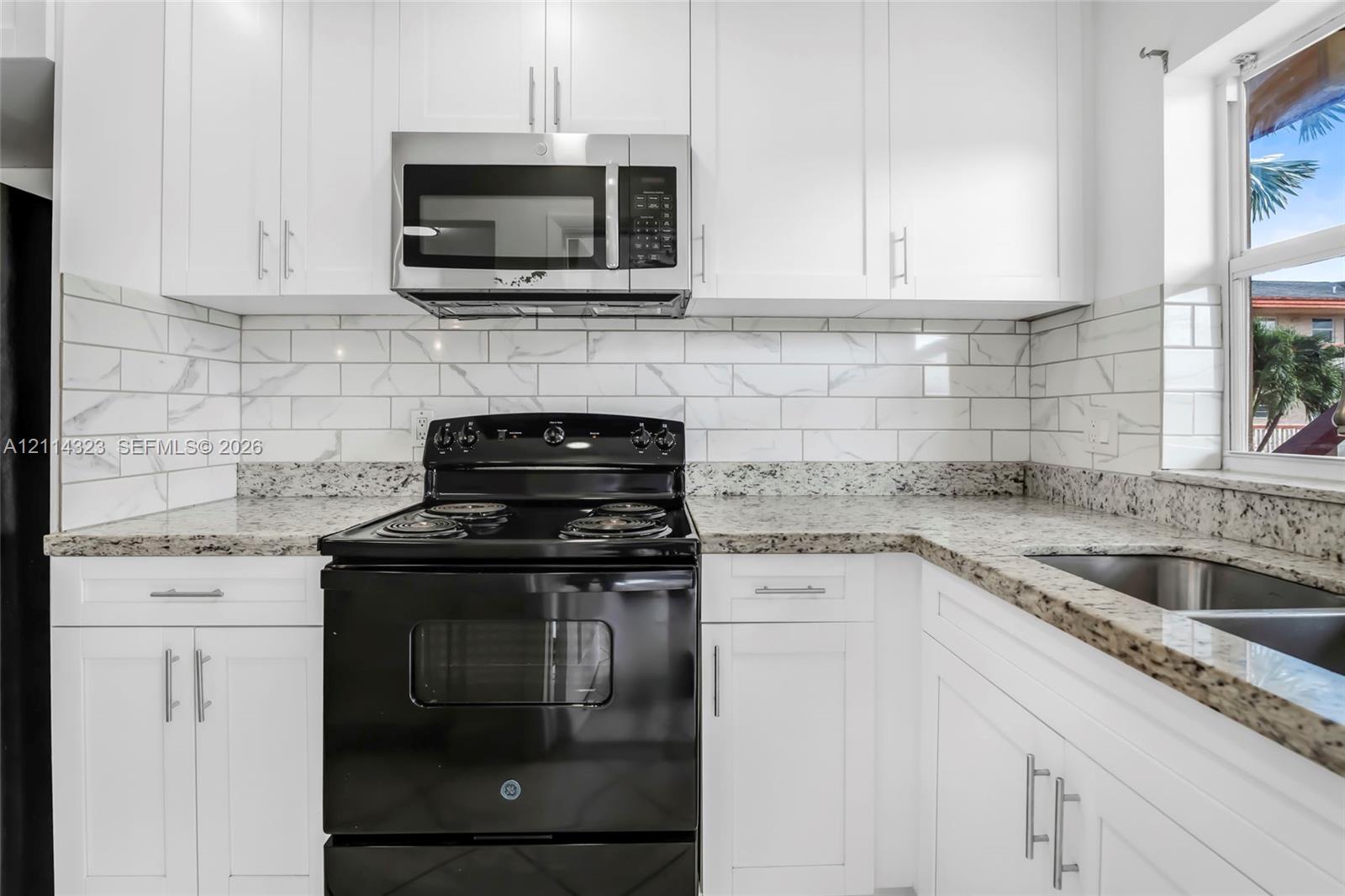 Kitchen featuring white Shaker-style cabinetry, stone-finish countertops, stainless steel microwave, black range, and stone-patterned subway tile backsplash
