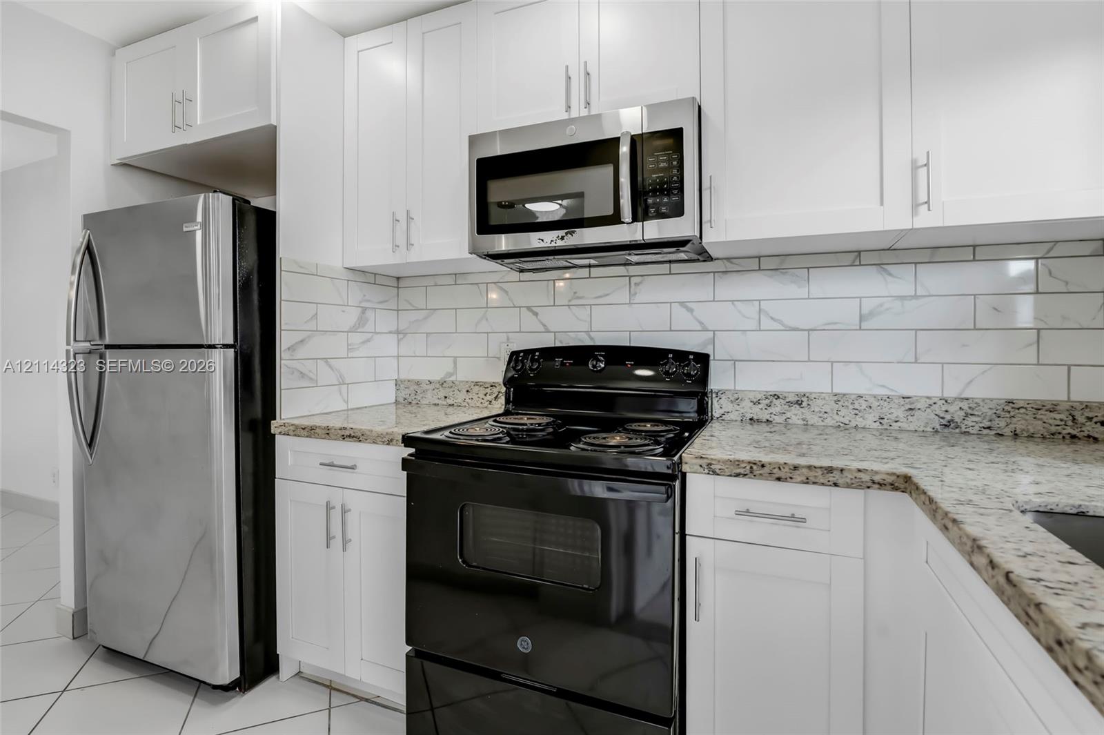 Kitchen featuring white shaker-style cabinetry, stone-finish countertops, subway tile backsplash, stainless steel microwave, and stone-tile flooring
