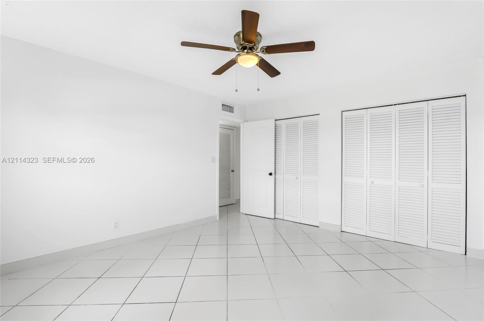 Room interior featuring white tile flooring, ceiling fan with integrated lighting, and multiple white louvered-style closet doors