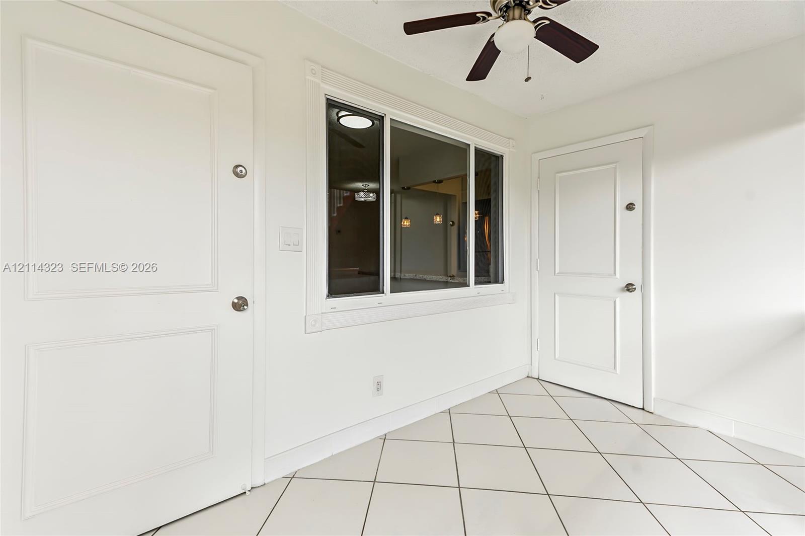 Diagonal tile flooring, two solid-panel doors, a central multi-pane window, and a ceiling-mounted light fixture with a fan