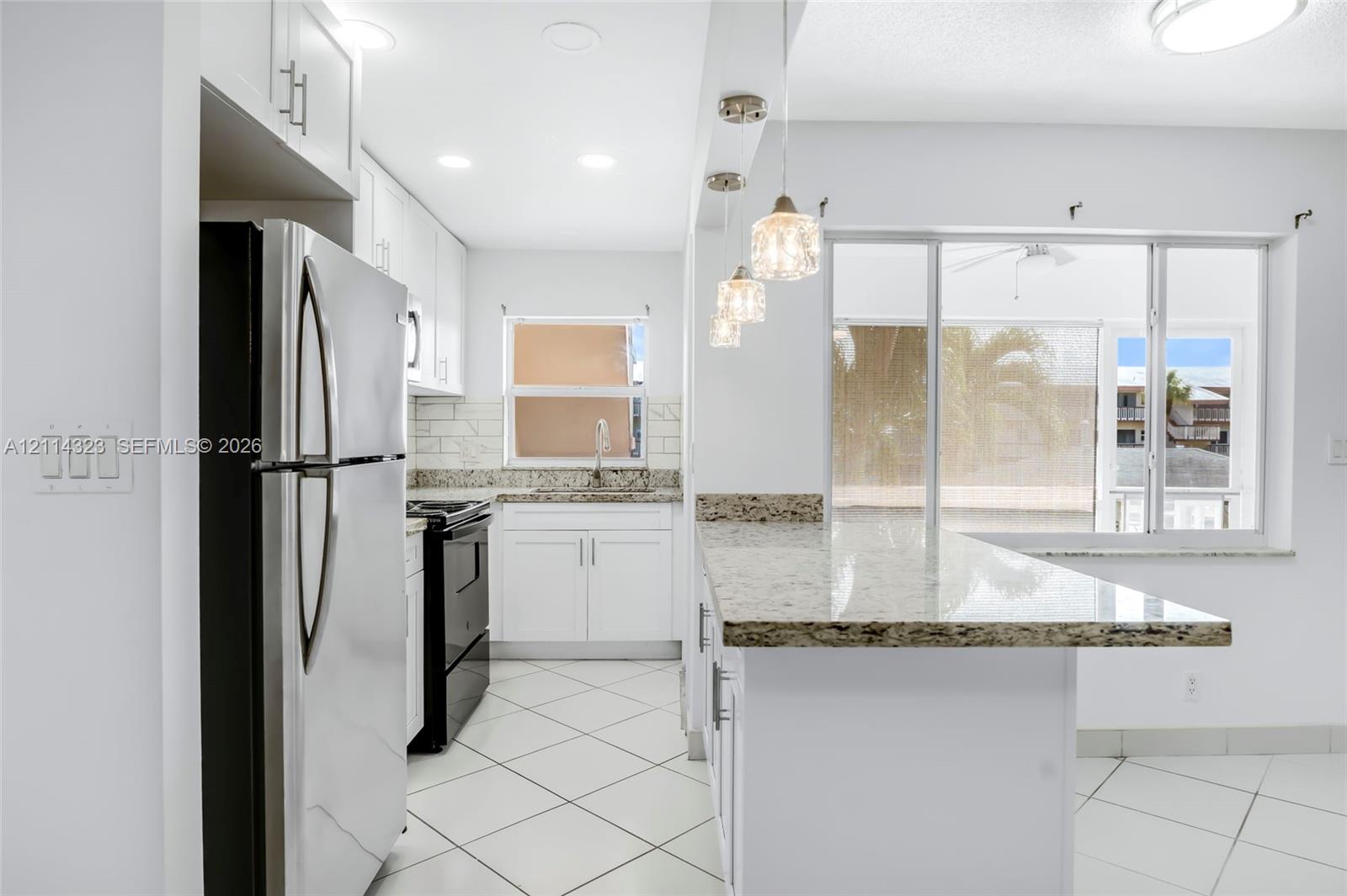 Kitchen featuring white shaker-style cabinetry, stone-finish countertops, tile flooring, subway tile backsplash, and decorative pendant lighting