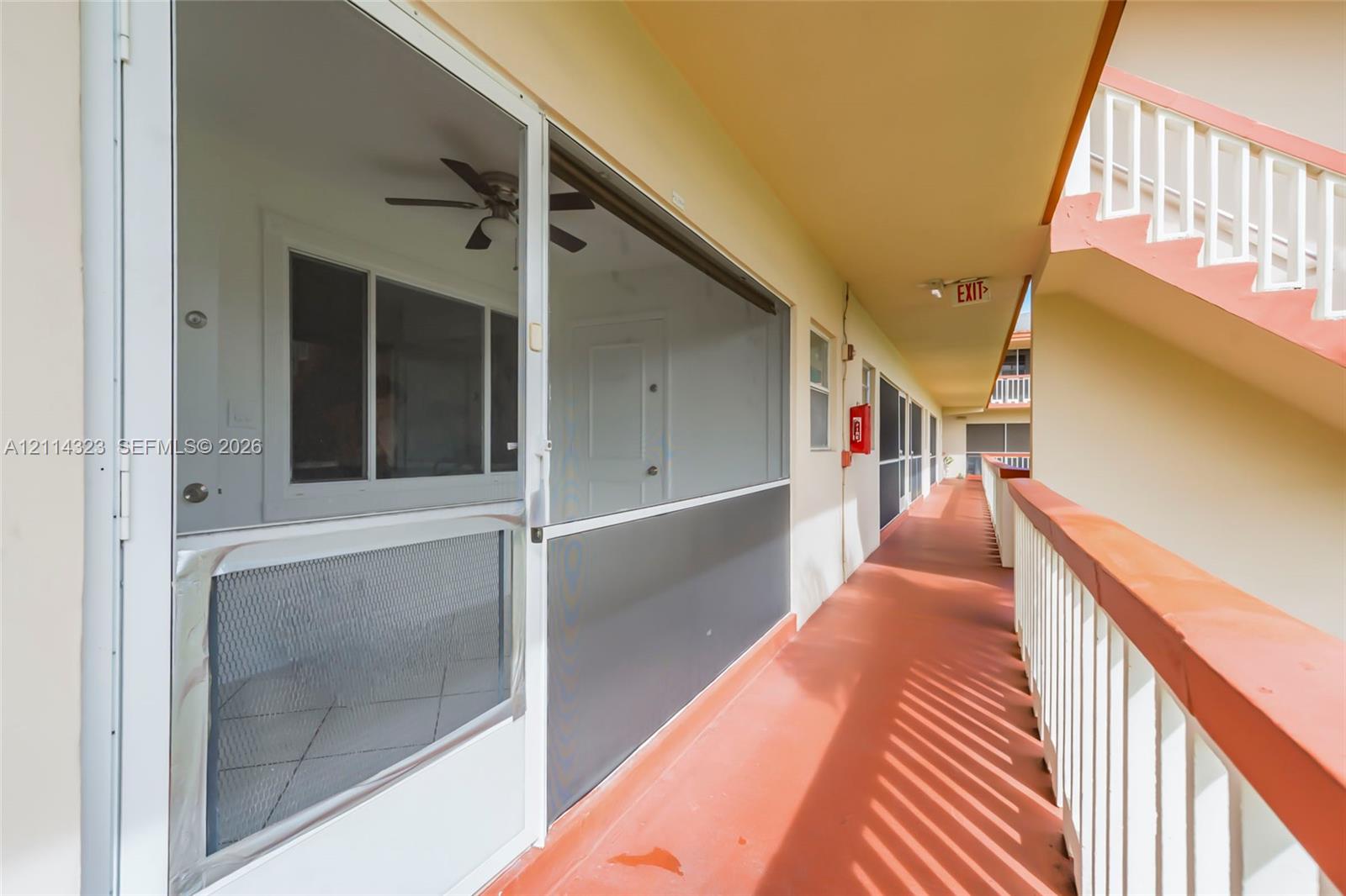 Covered exterior corridor featuring a white metal screen door, painted flooring, and a white balustrade staircase