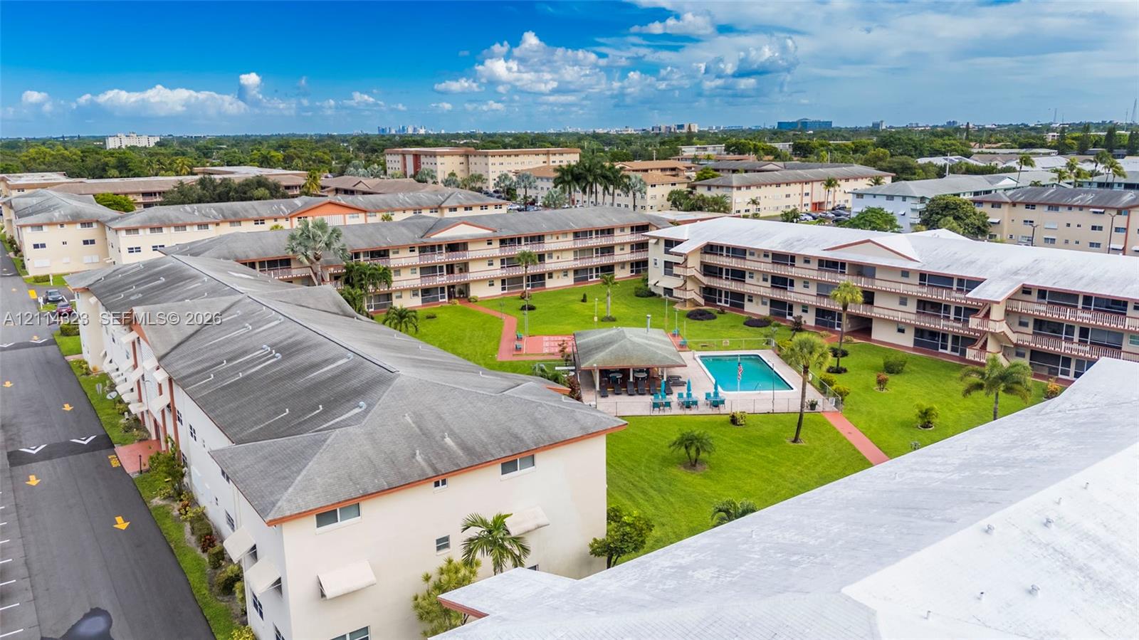 Multi-building complex featuring a central courtyard with a swimming pool, shaded pavilion, landscaped grounds, and paved walkways
