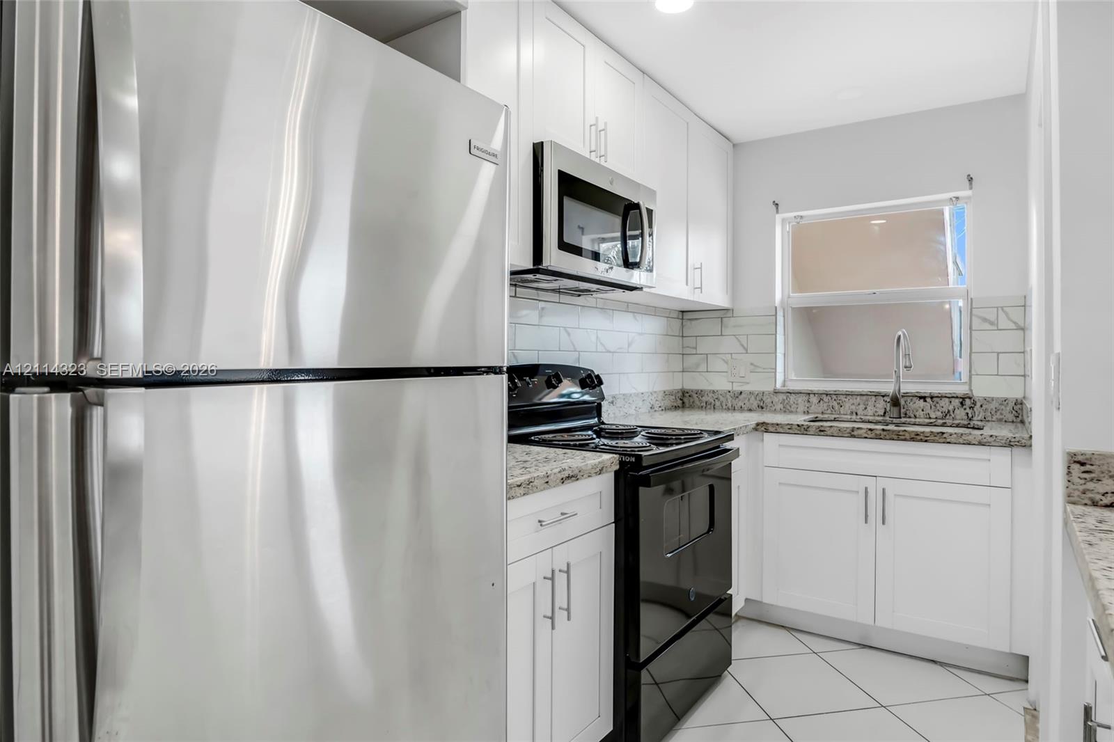 Kitchen featuring white shaker-style cabinetry, stone-finish countertops, subway tile backsplash, stainless steel refrigerator, and built-in microwave