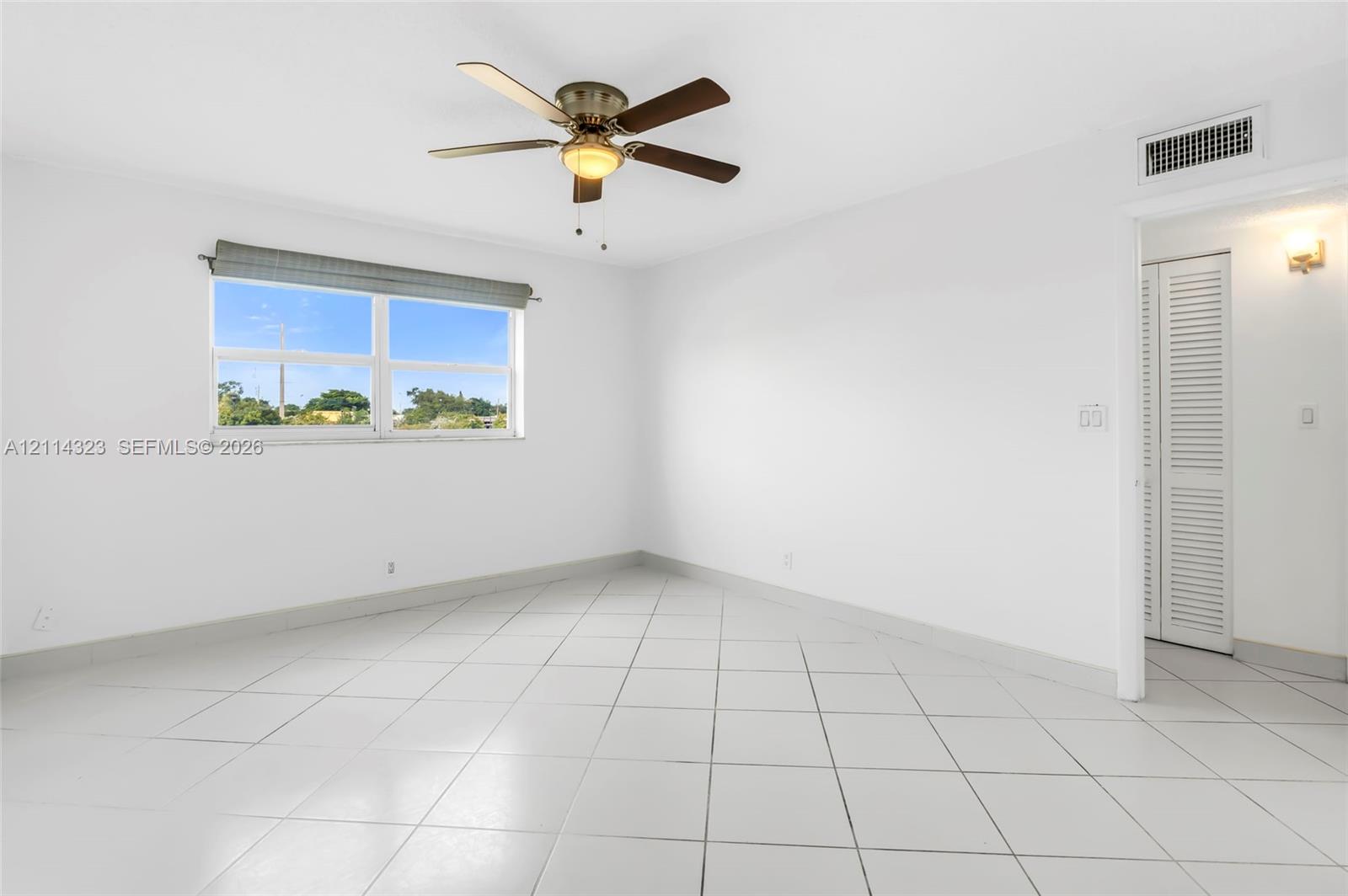 Interior room featuring neutral ceramic tile flooring, a multi-blade ceiling fan with integrated lighting, and louvered closet doors