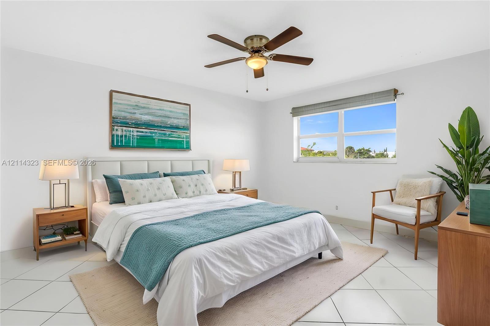 VIRTUALLY STAGED Room featuring white ceramic tile flooring, a multi-blade ceiling fan with integrated lighting, and a large window with a roller shade