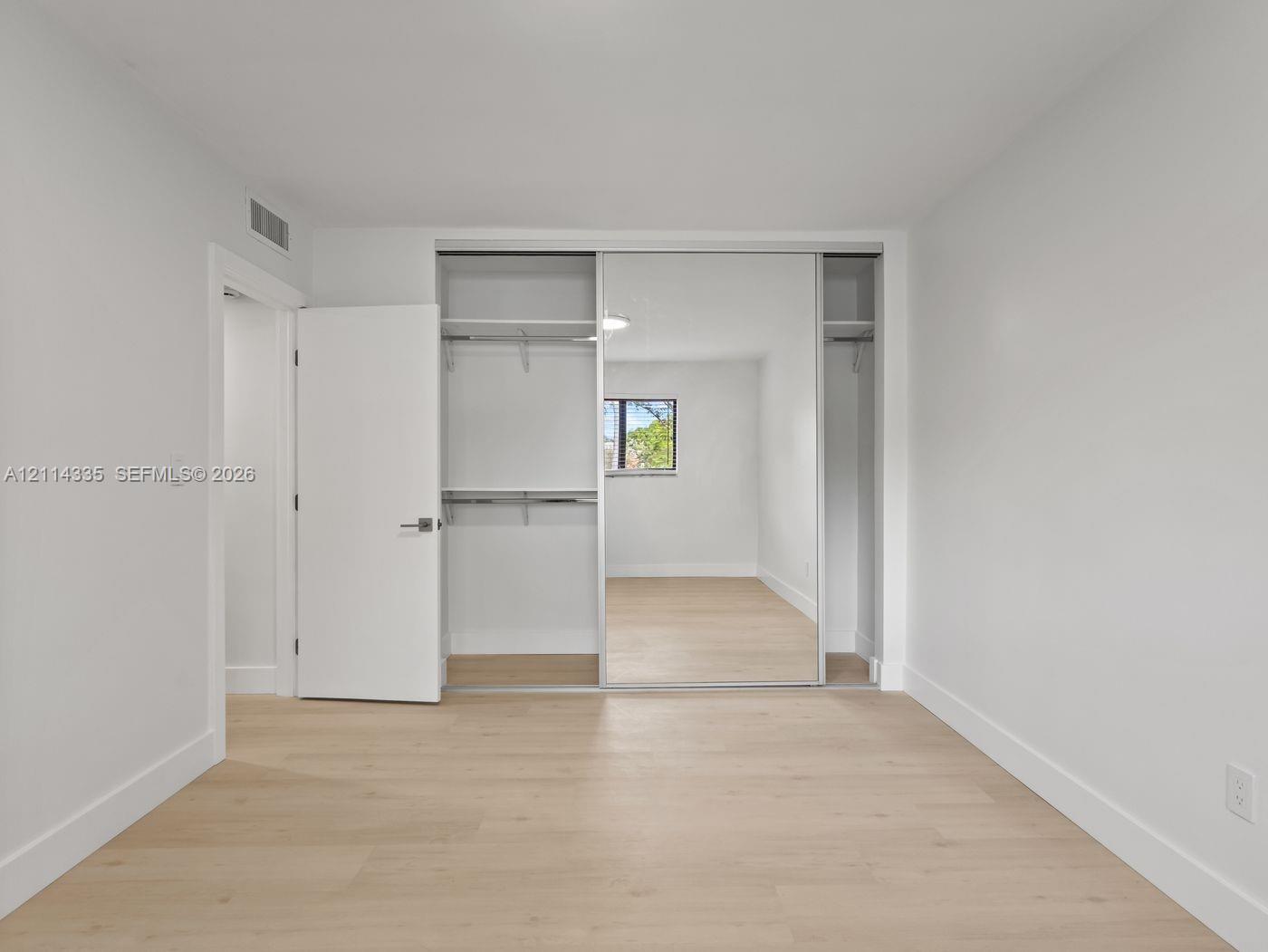 Neutral-toned interior featuring wood-finish flooring, sliding mirror-door closet with built-in shelving, and a solid-core swing door