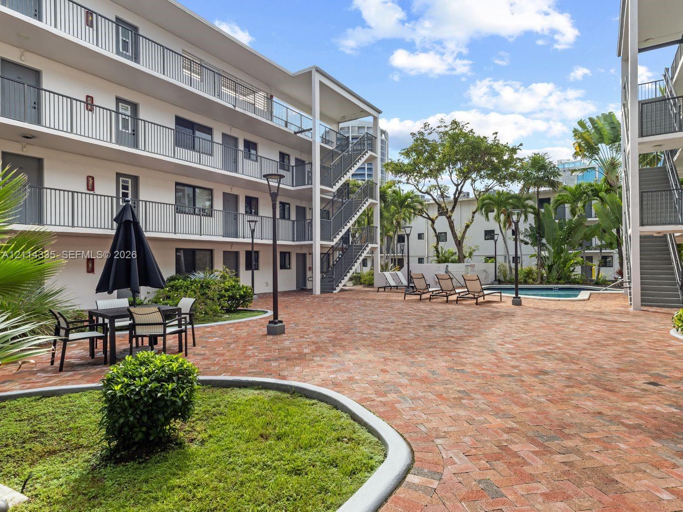 Courtyard featuring brick paver hardscaping, swimming pool, mature palm trees, multi-level metal staircases, and exterior catwalks