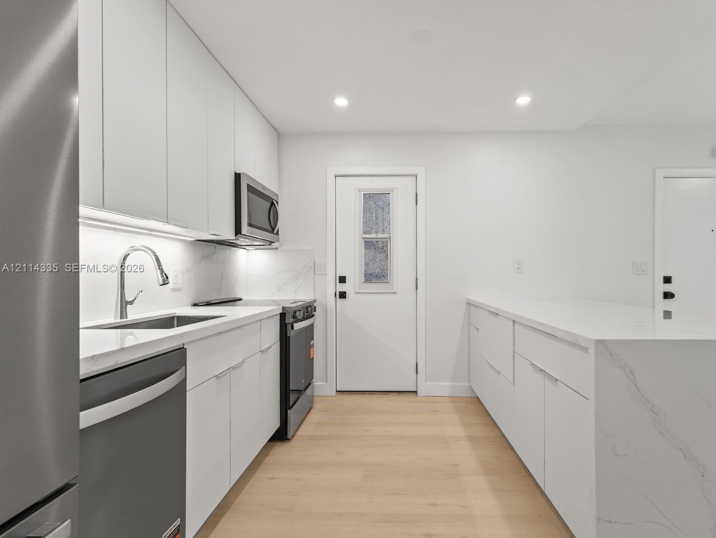 Kitchen featuring flat-panel cabinetry, light-toned stone-finish countertops, stainless steel appliances, and wood-finish flooring