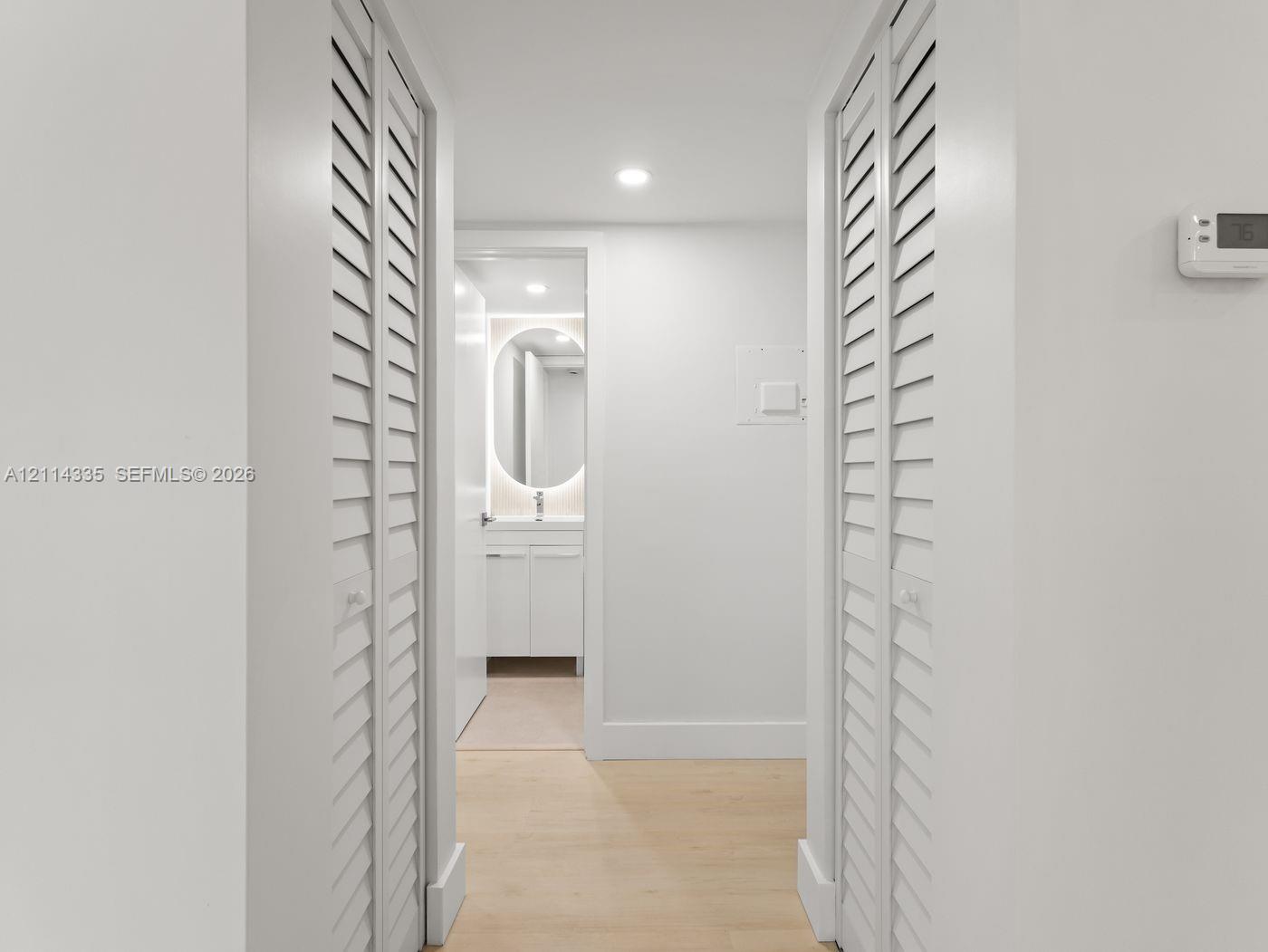 Interior hallway featuring dual white louvered closet doors, recessed ceiling lighting, and wood-finish flooring
