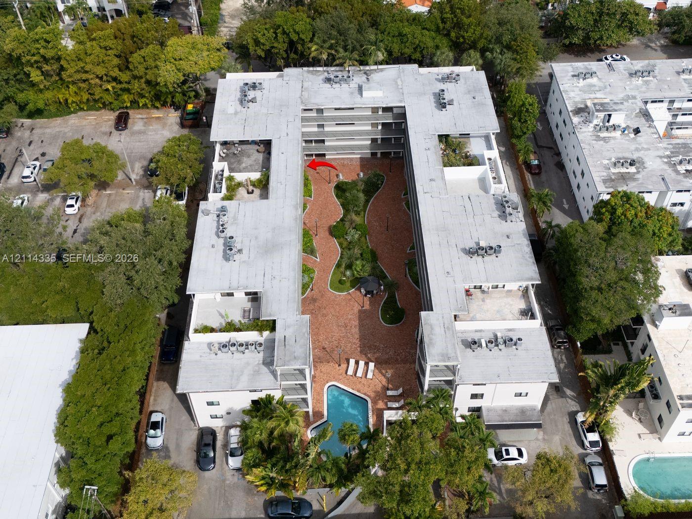 Multi-story residential complex featuring a central courtyard with paved walkways, manicured landscaping, and an outdoor swimming pool