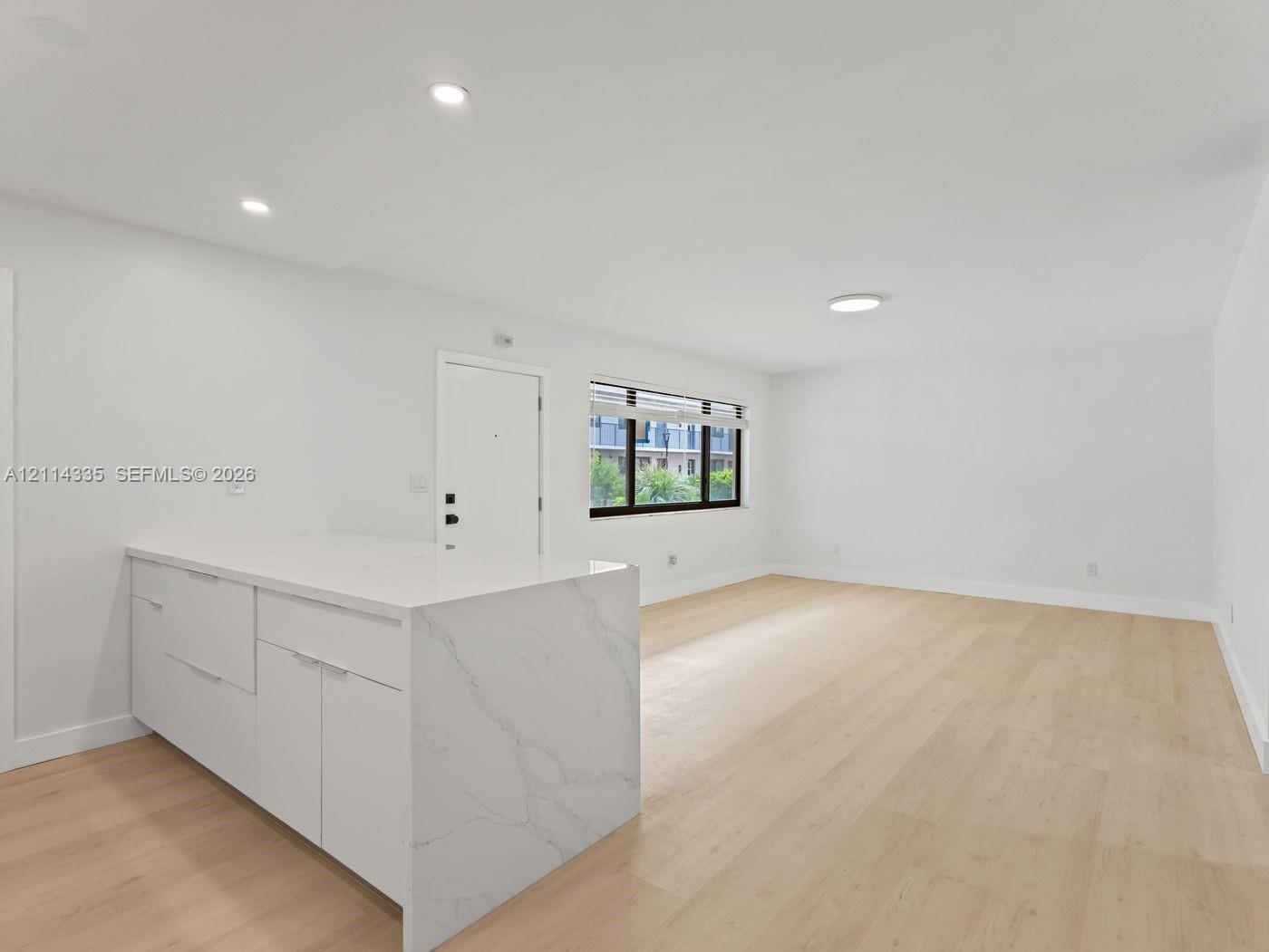 Open-concept interior featuring light wood-finish flooring, white cabinetry with a waterfall edge stone countertop, and recessed lighting