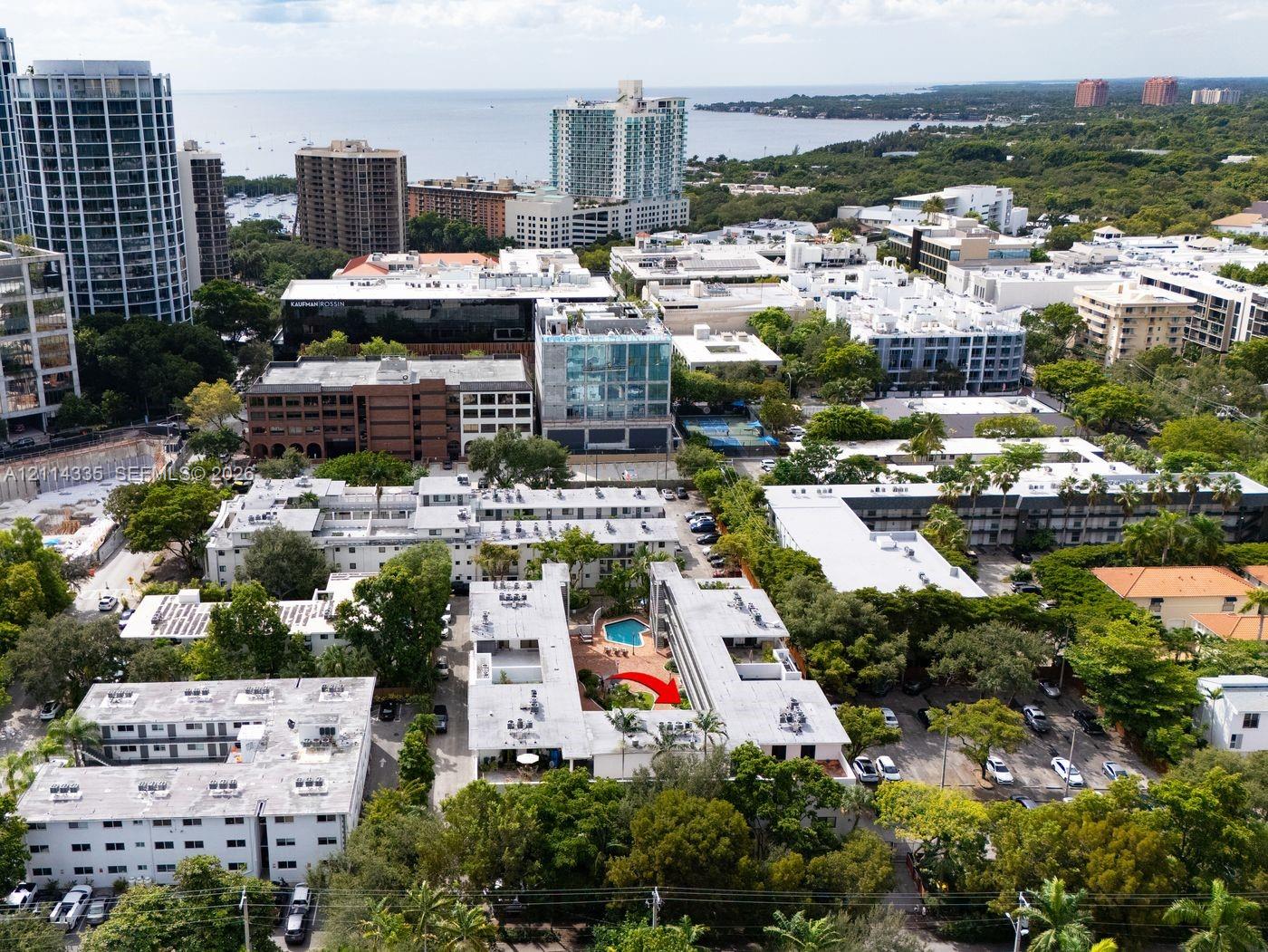 Aerial perspective of a multi-unit complex featuring an in-ground courtyard swimming pool, mature perimeter landscaping, and surface parking