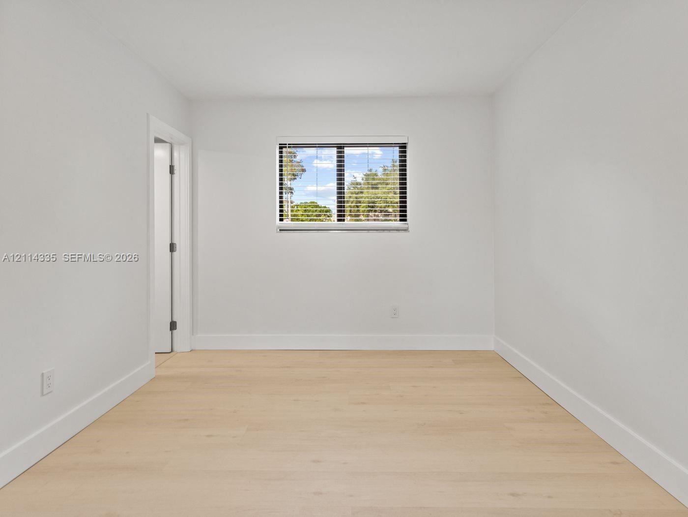 Interior space featuring wood-finish flooring, neutral walls, and a single-pane window with integrated blinds