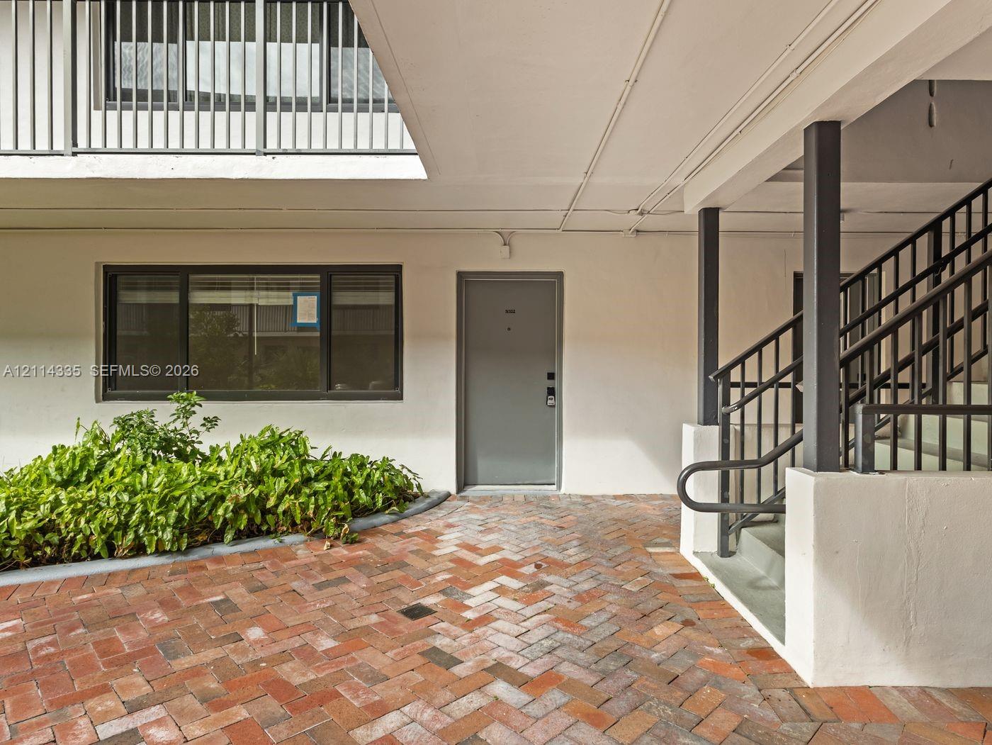 Herringbone brick courtyard featuring a metal staircase, smooth stucco exterior walls, dark-framed windows, and integrated landscaping
