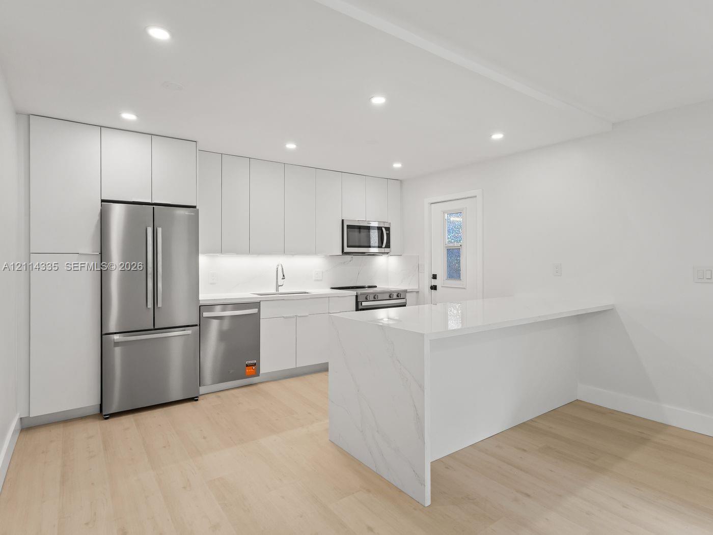 Modern kitchen featuring floor-to-ceiling cabinetry, a waterfall-edge island, integrated stainless steel appliances, recessed lighting, and wood-finish flooring