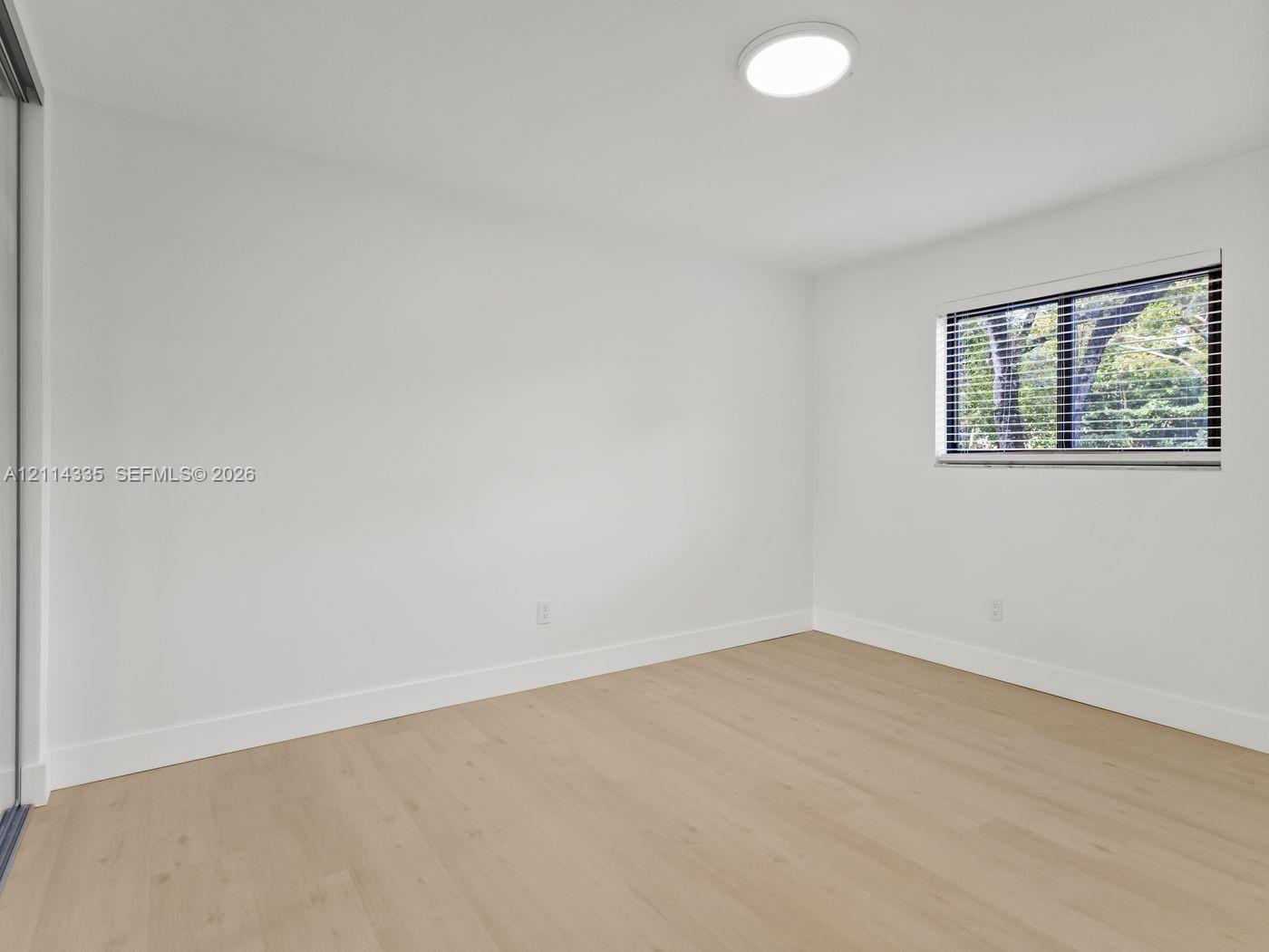 Interior space featuring wood-finish flooring, neutral walls, recessed LED lighting, and a window equipped with horizontal blinds