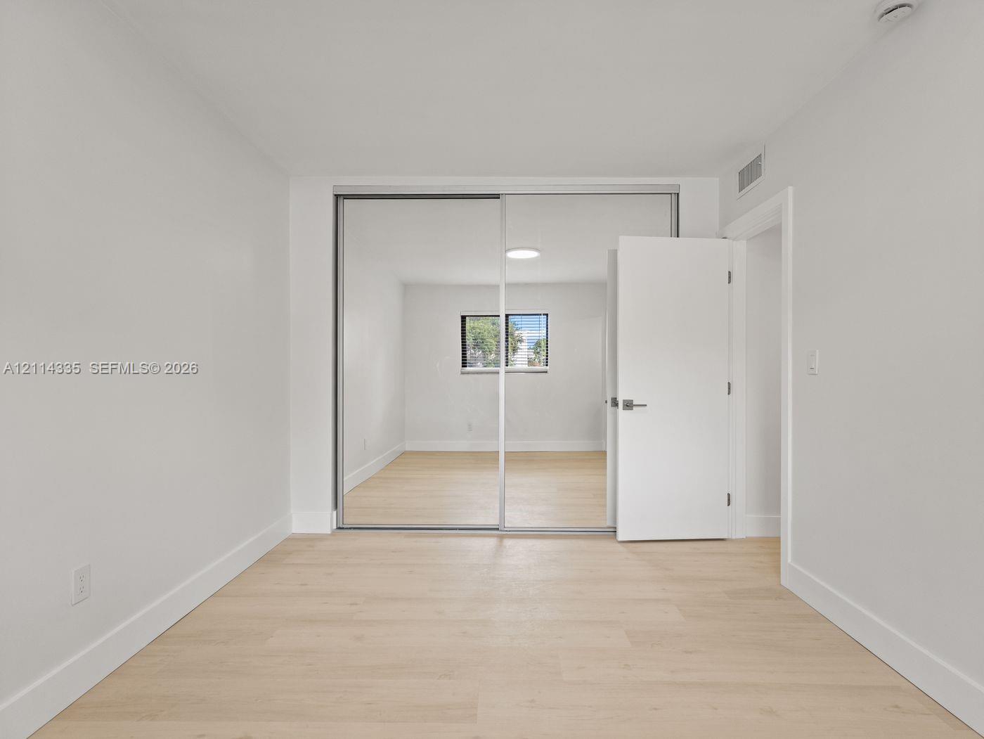 Interior room featuring light wood-finish flooring, white walls, and floor-to-ceiling mirrored sliding closet doors