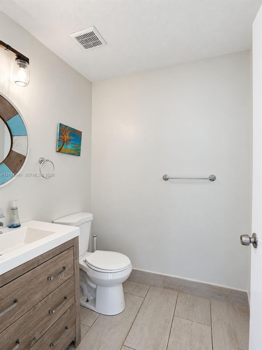 Bathroom featuring a wood-finish vanity with an integrated rectangular sink, large-format tile flooring, a wall-mounted metal towel bar, and a multi-light fixture