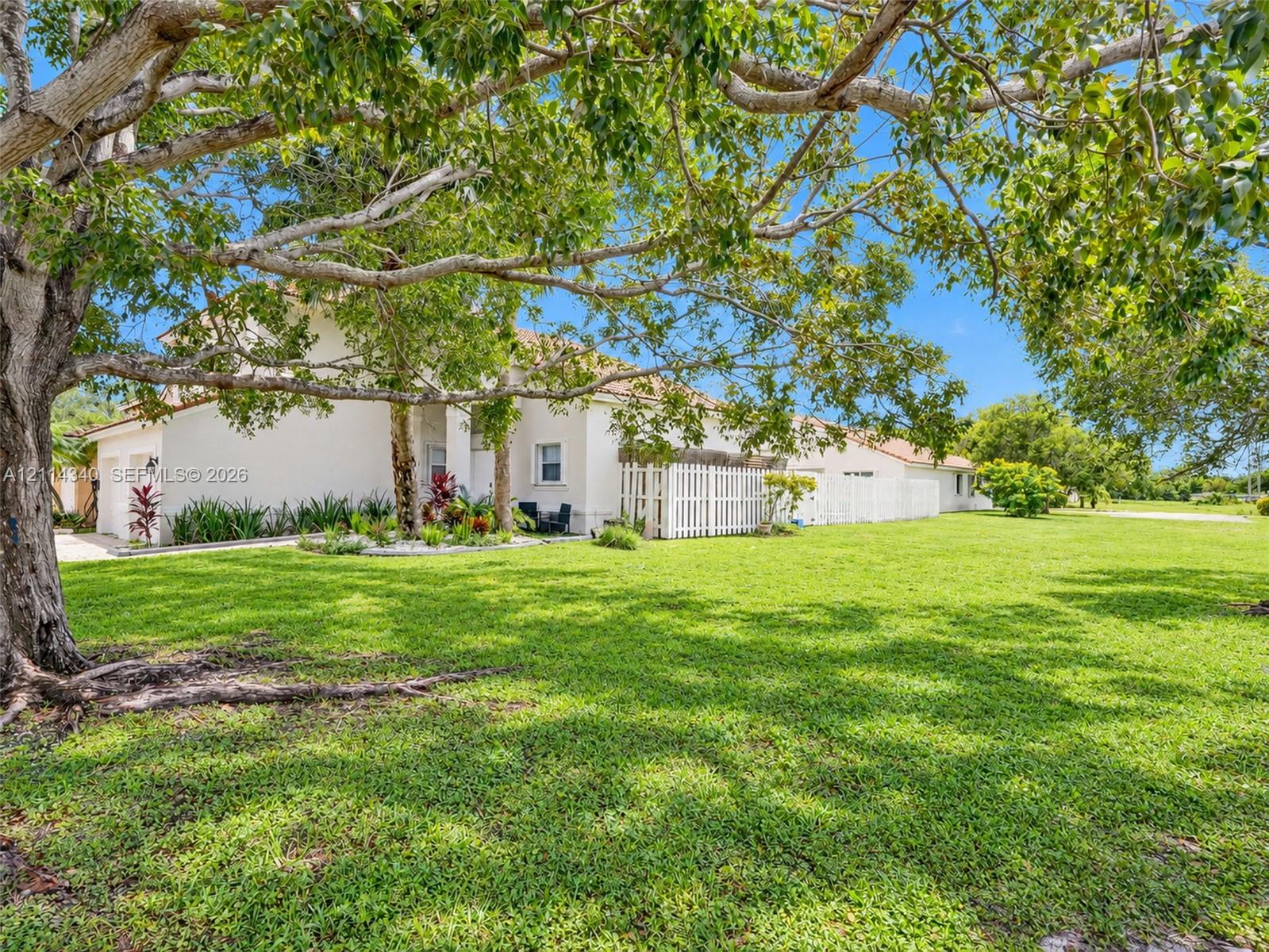 Expansive lot featuring mature shade trees, established landscaping, and a white privacy fence