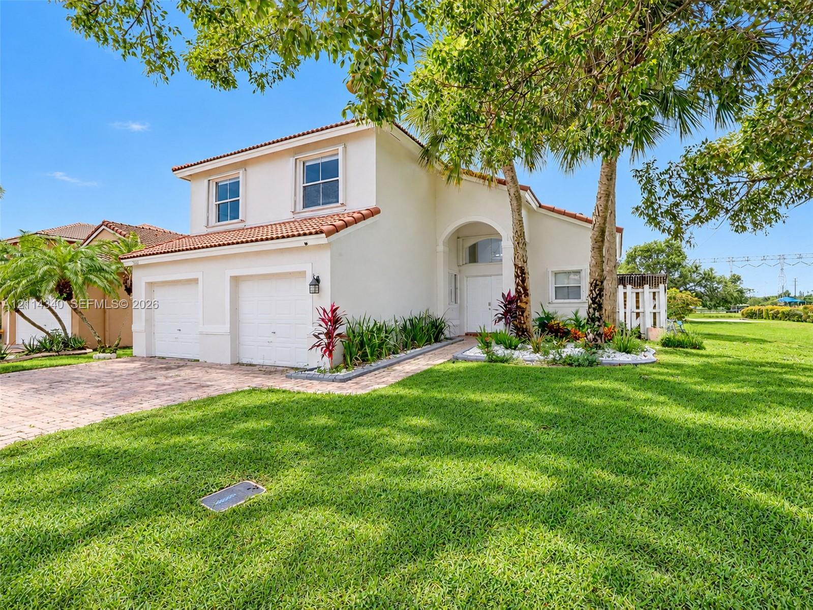 Stucco exterior residence featuring a terracotta-tile roof, two-car garage, arched entryway, and paver driveway