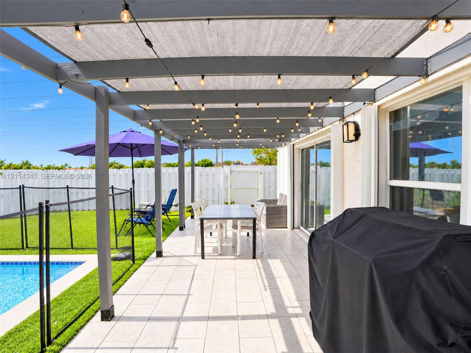 Outdoor patio featuring a gray-painted wood pergola with a sunshade canopy, tile flooring, and integrated string lighting