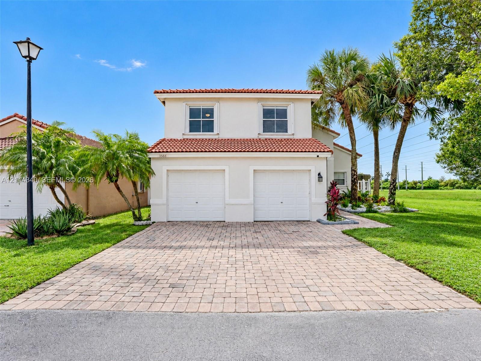 Two-story exterior featuring a light stucco facade, terracotta-tiled roof, double-car garage, and a paved brick driveway