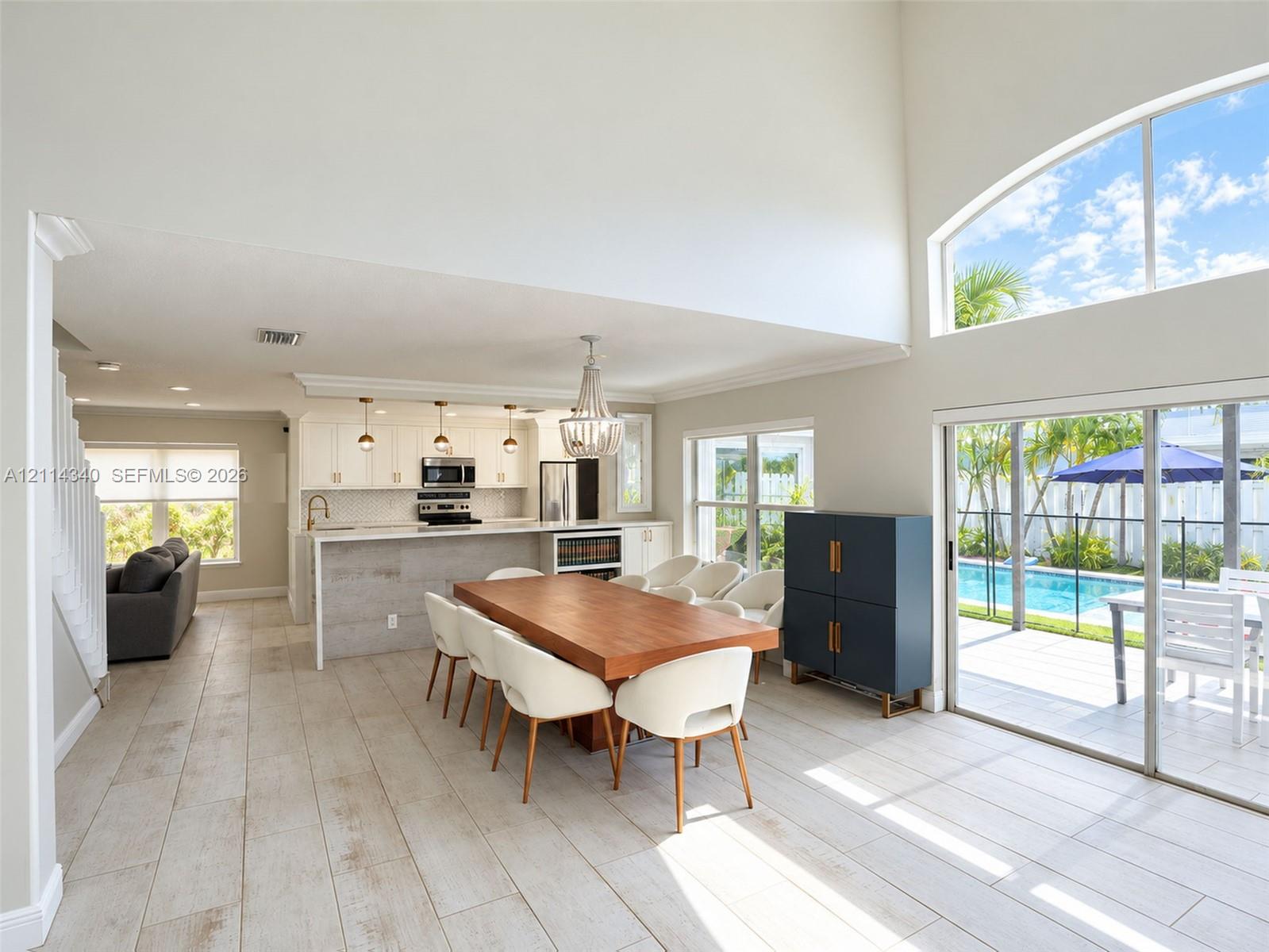 Open-concept floor plan featuring high ceilings, wood-finish tile flooring, a chef's kitchen with a stone-top island, and large sliding glass doors providing outdoor access