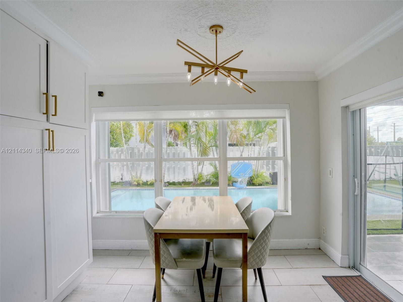 Dining area featuring built-in floor-to-ceiling cabinetry with metallic hardware, large multi-pane windows, gold-tone modern chandelier, and oversized ceramic tile flooring