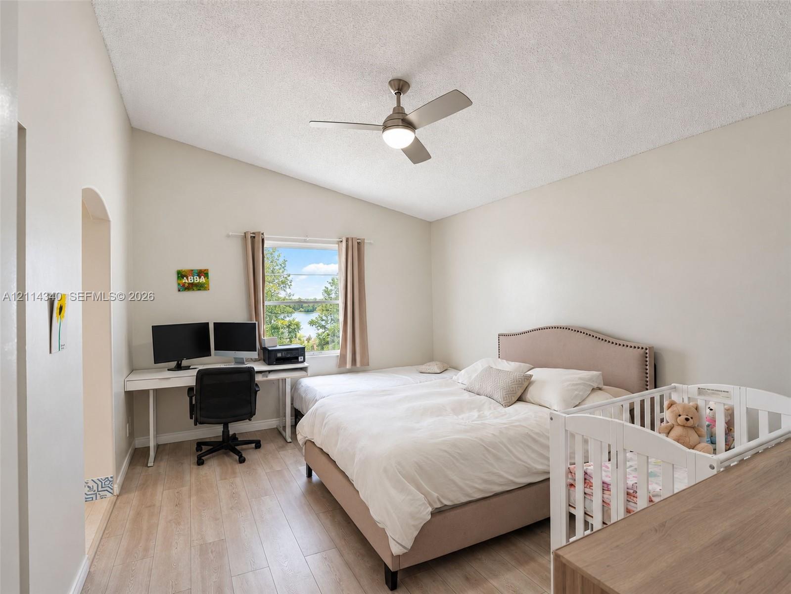 Vaulted ceiling featuring a central brushed-metal ceiling fan with integrated light, wood-finish flooring, and natural light from a window with exterior water surroundings