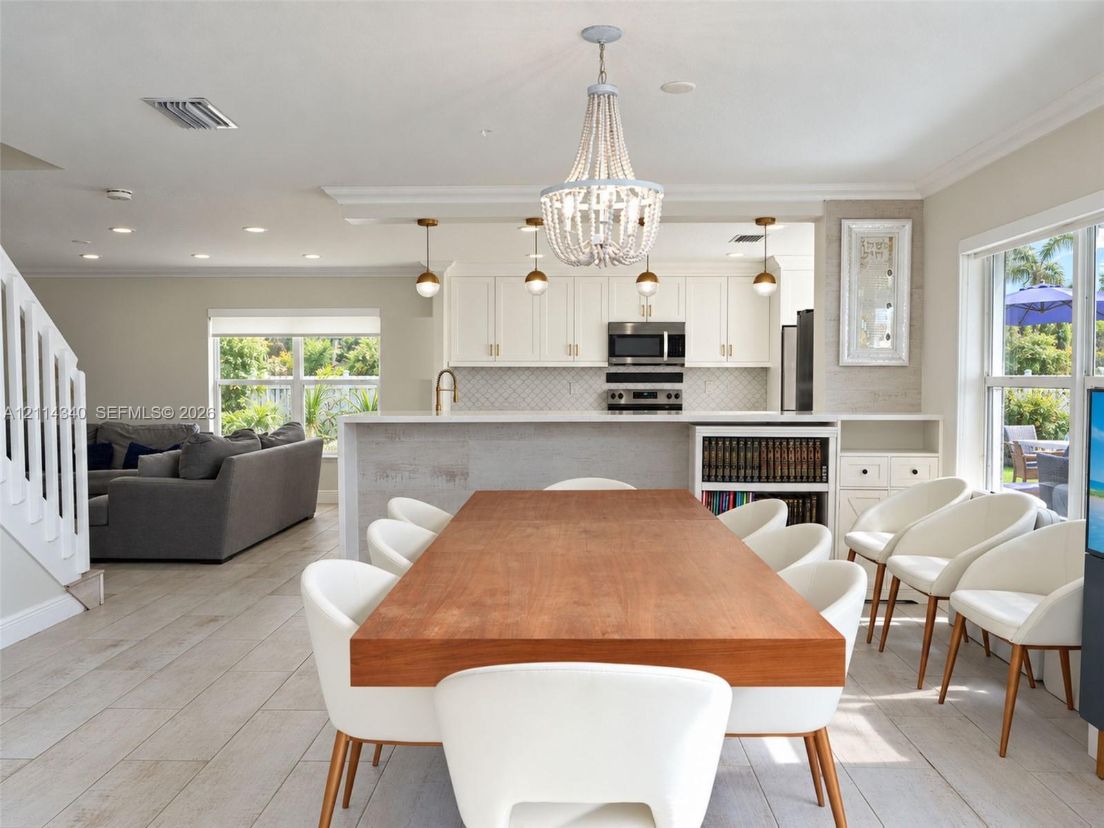 Kitchen featuring white shaker-style cabinetry, a quartz countertop island, stone-patterned backsplash, wood-finish flooring, and a decorative bead-frame chandelier
