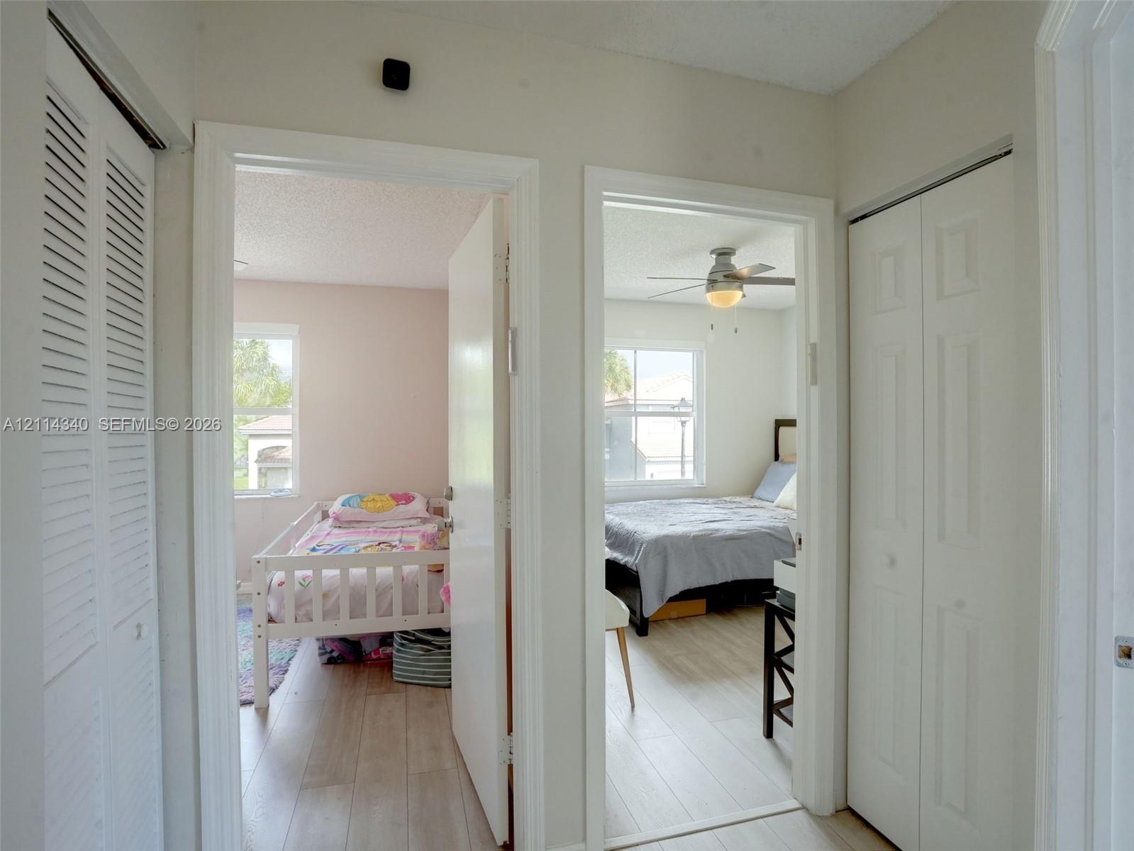 Hallway featuring two sets of white louvered-style bi-fold closet doors, wood-finish flooring, and two interior doorways with light-colored solid-core doors