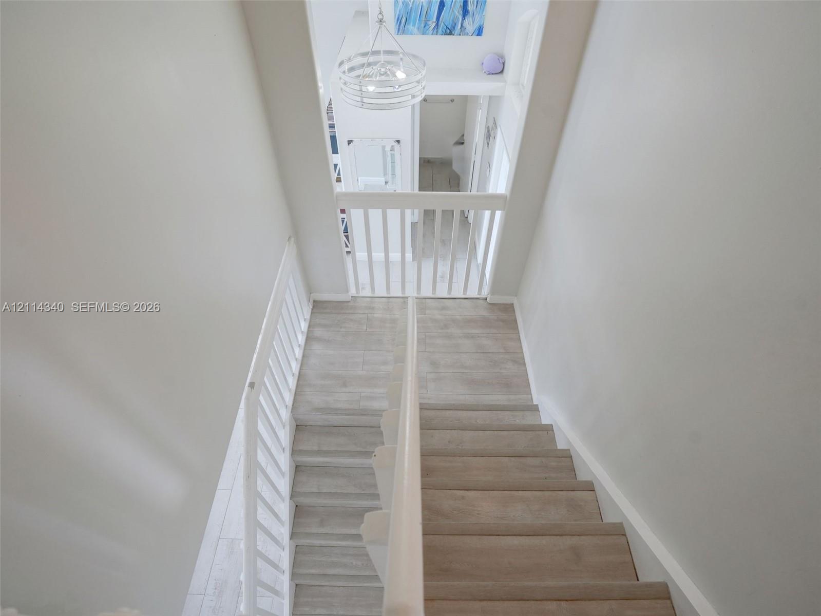 Staircase featuring wood-finish treads, white painted balustrades, and a tiered drum chandelier