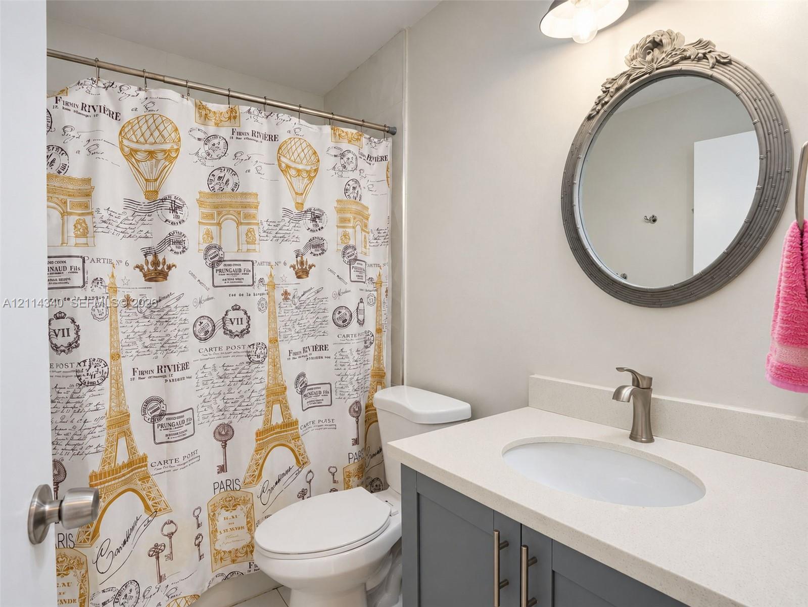 Bathroom featuring a vanity with shaker-style cabinetry, light-toned countertop, integrated oval sink, brushed-finish faucet, and an ornate circular wall mirror