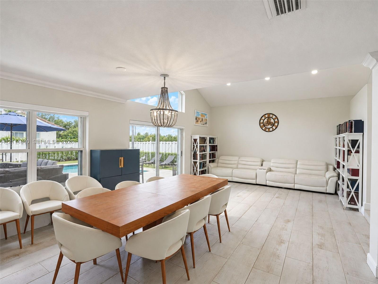 Vaulted ceilings with recessed lighting, wood-finish tile flooring, a statement chandelier, and large sliding glass doors providing natural light