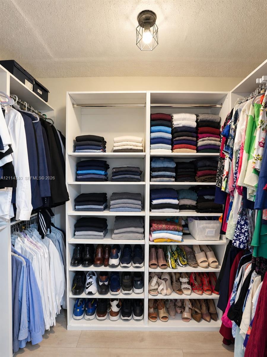 Walk-in closet featuring white built-in shelving, multiple hanging rods, and an industrial-style geometric flush mount light fixture