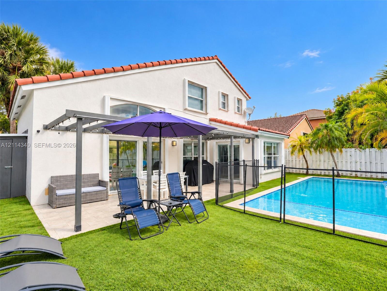 Stucco exterior with a tiled roof, featuring a covered patio, swimming pool, and artificial turf lawn