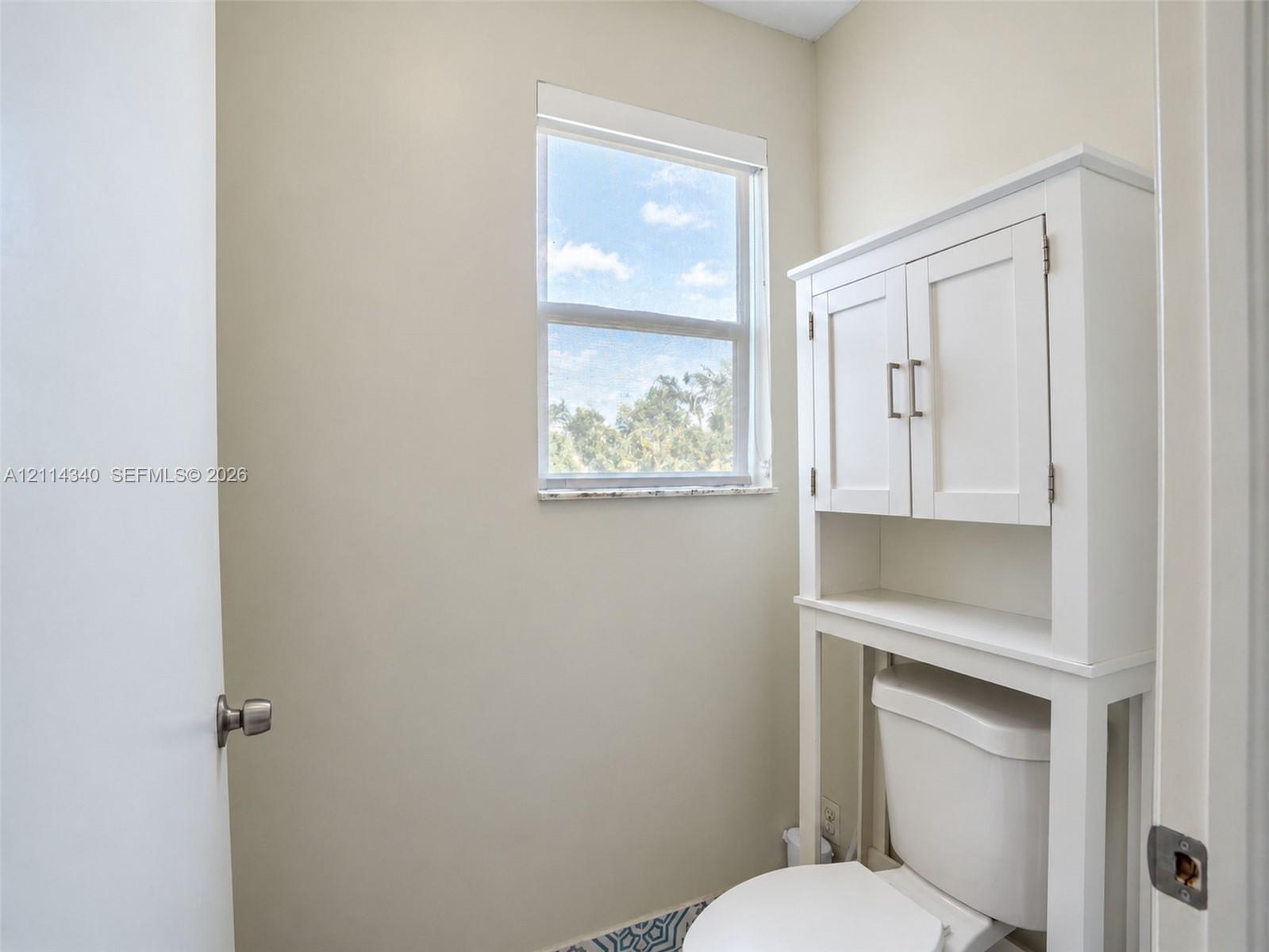 Single-pane window with a stone-finish sill, built-in over-the-toilet storage cabinetry, and patterned tile flooring